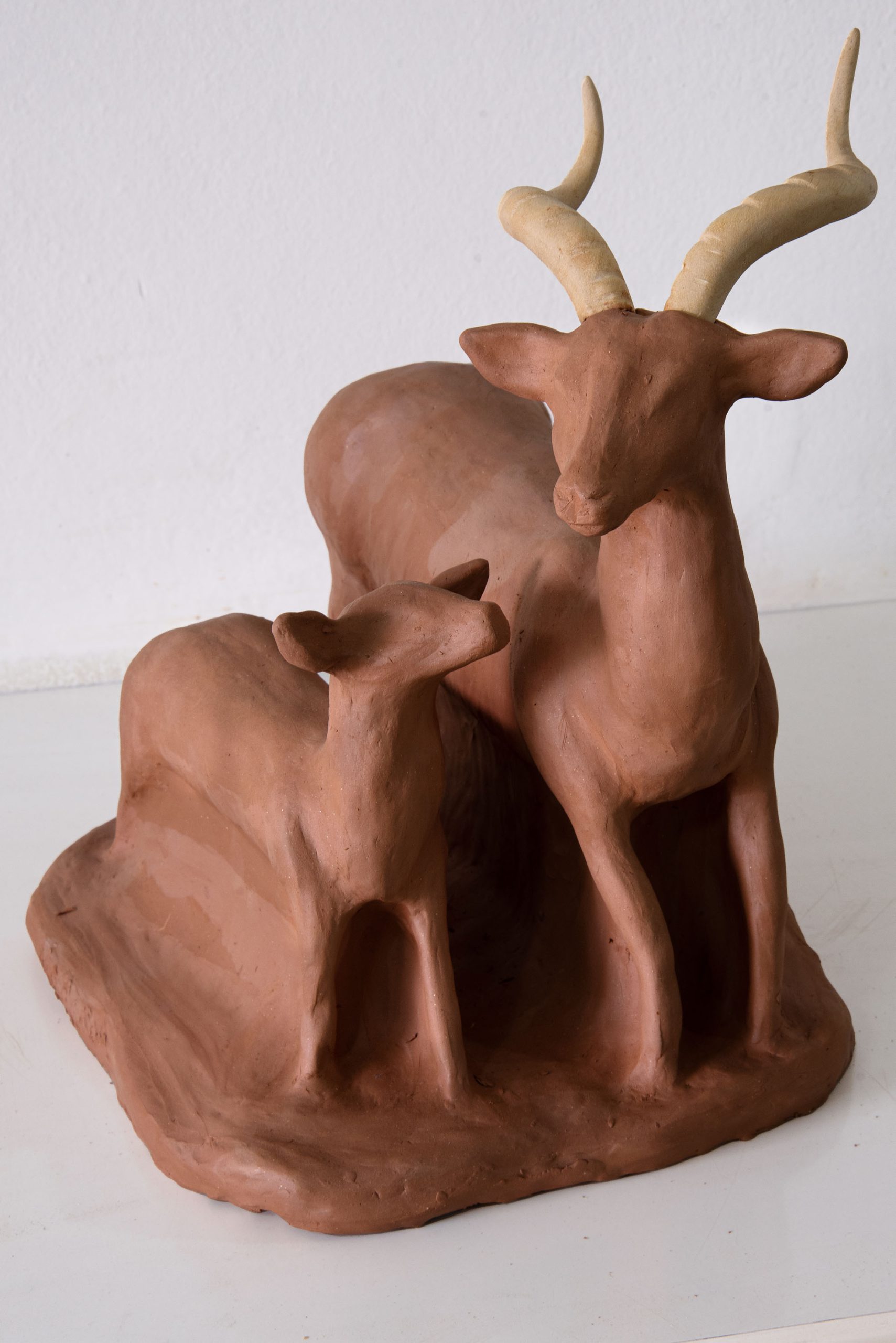 Escultura de argila marrom de veado adulto com chifres e filhote ao lado.