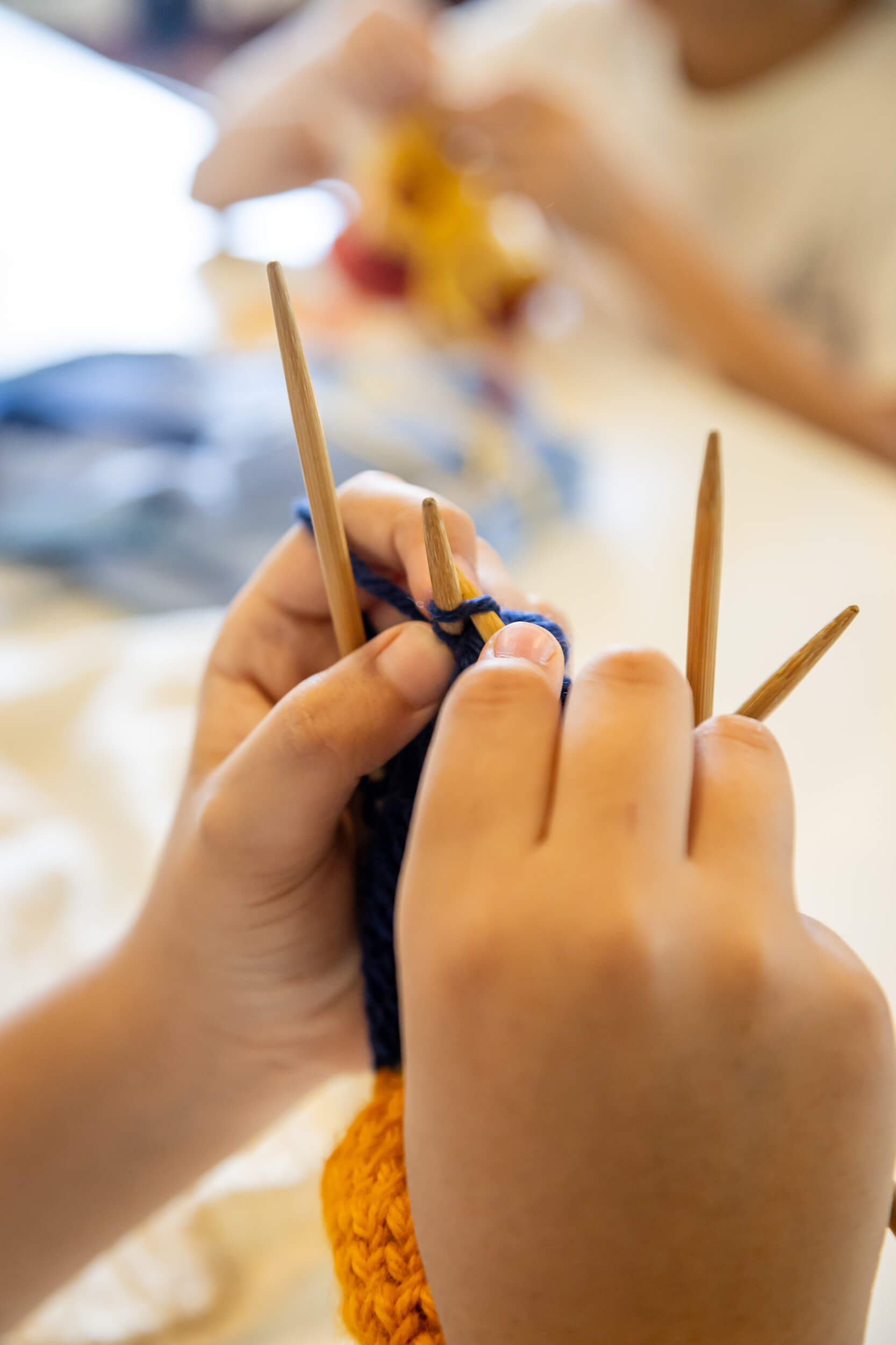 Mãos de criança tricotando com agulhas de madeira e fio de lã azul escuro em aula de trabalho manuais no Ensino Fundamental da Escola Waldorf Rudolf Steiner.