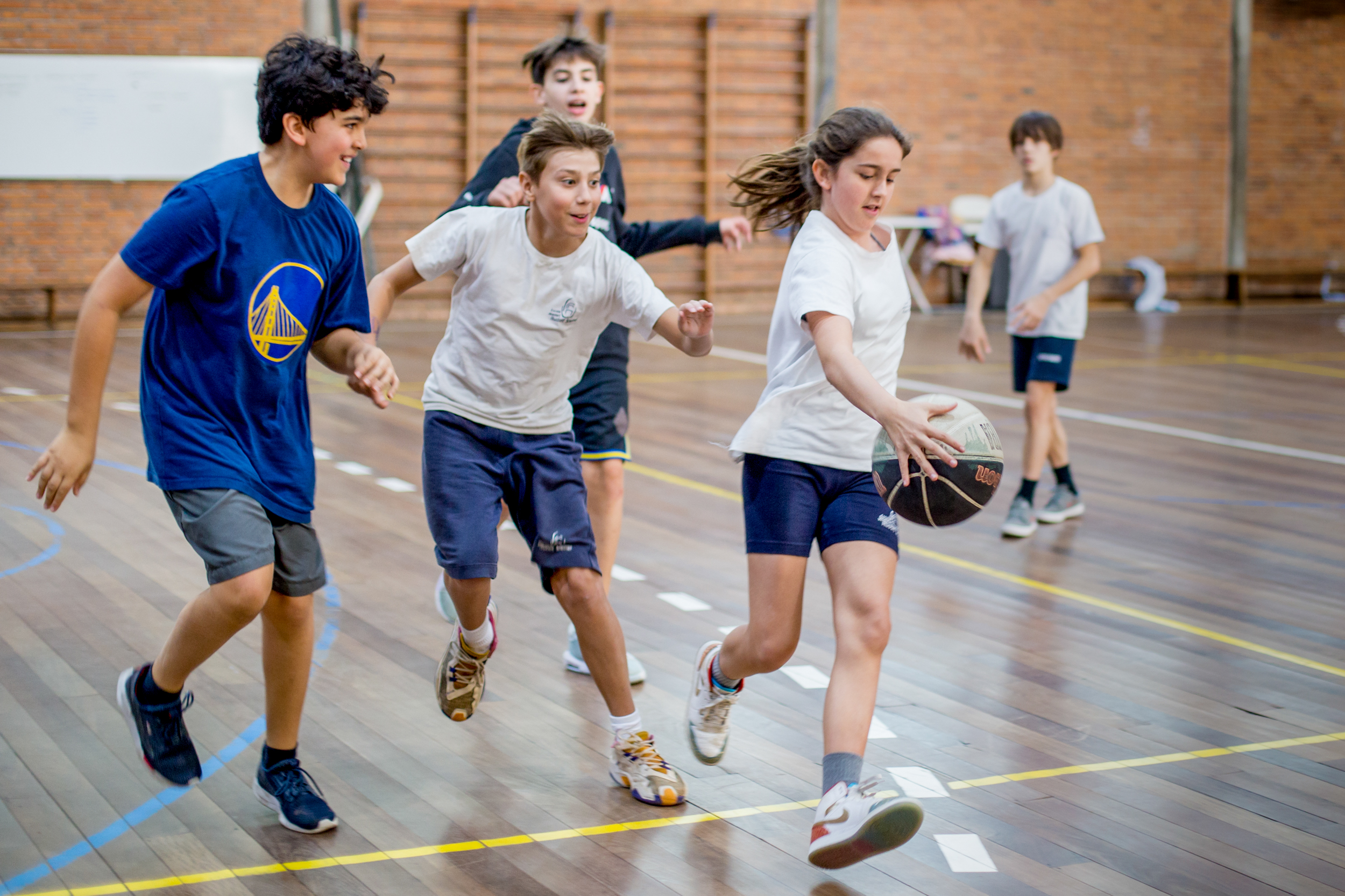 Adolescentes jogando basquete com menina driblando a bola em quadra interna