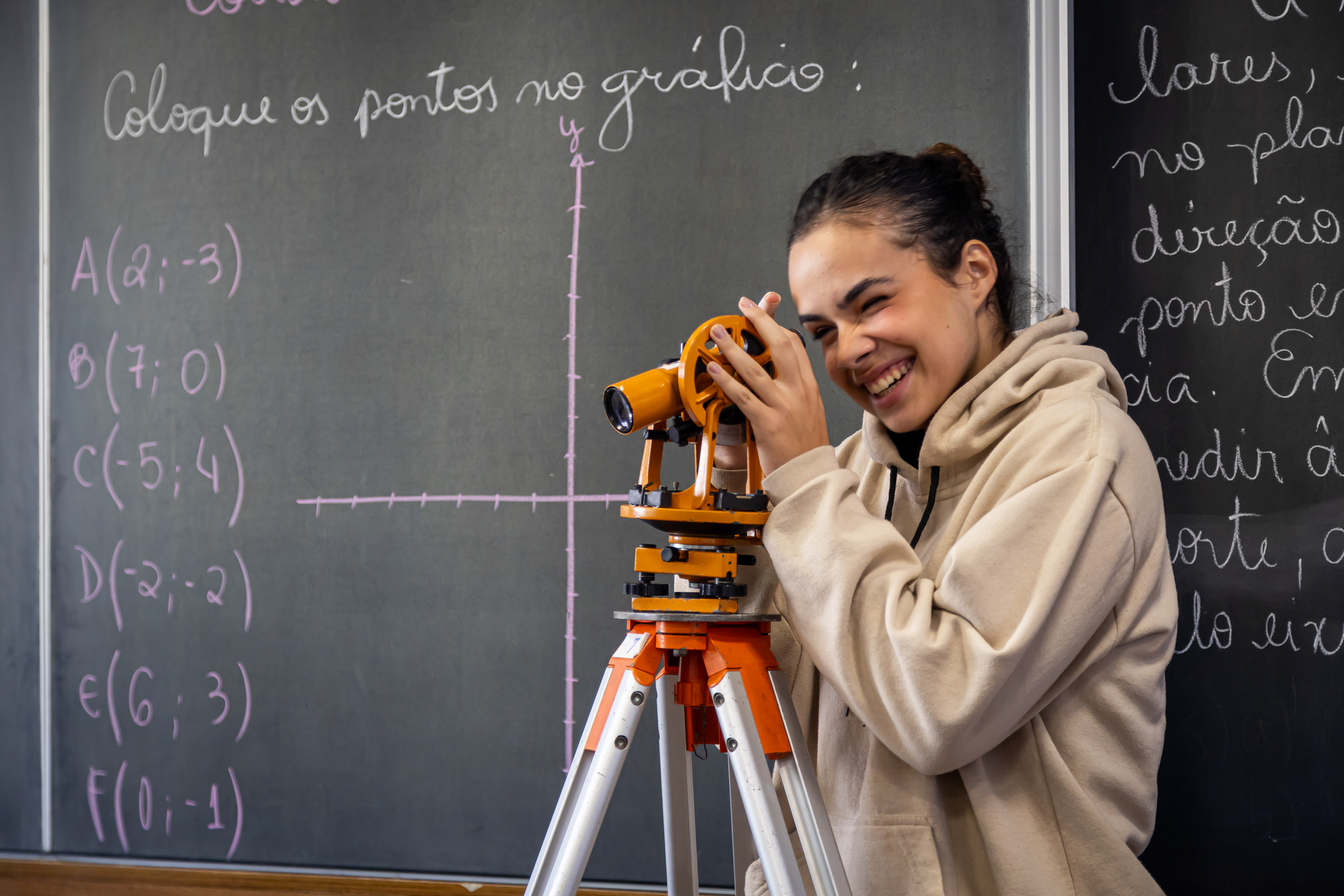 Aluna sorrindo usando teodolito em aula de matemática ou topografia na Escola Waldorf Rudolf Steiner.