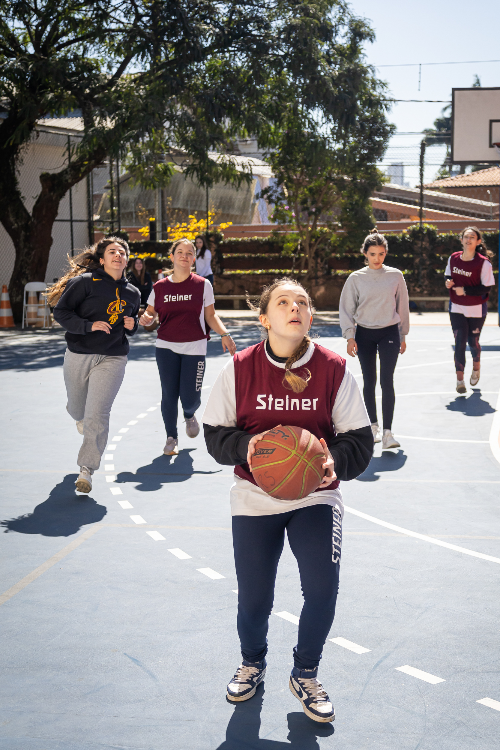 Alunas jogando basquete em quadra escolar na Escola Waldorf Rudolf Steiner, durante aula de educação física.