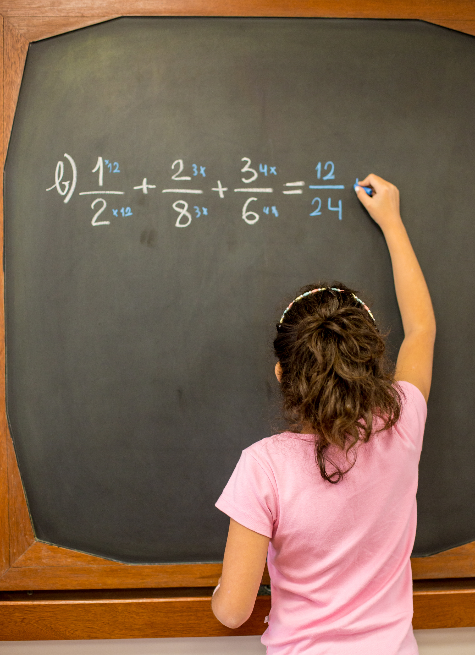 Criança escrevendo equação de matemática com frações em quadro-negro
