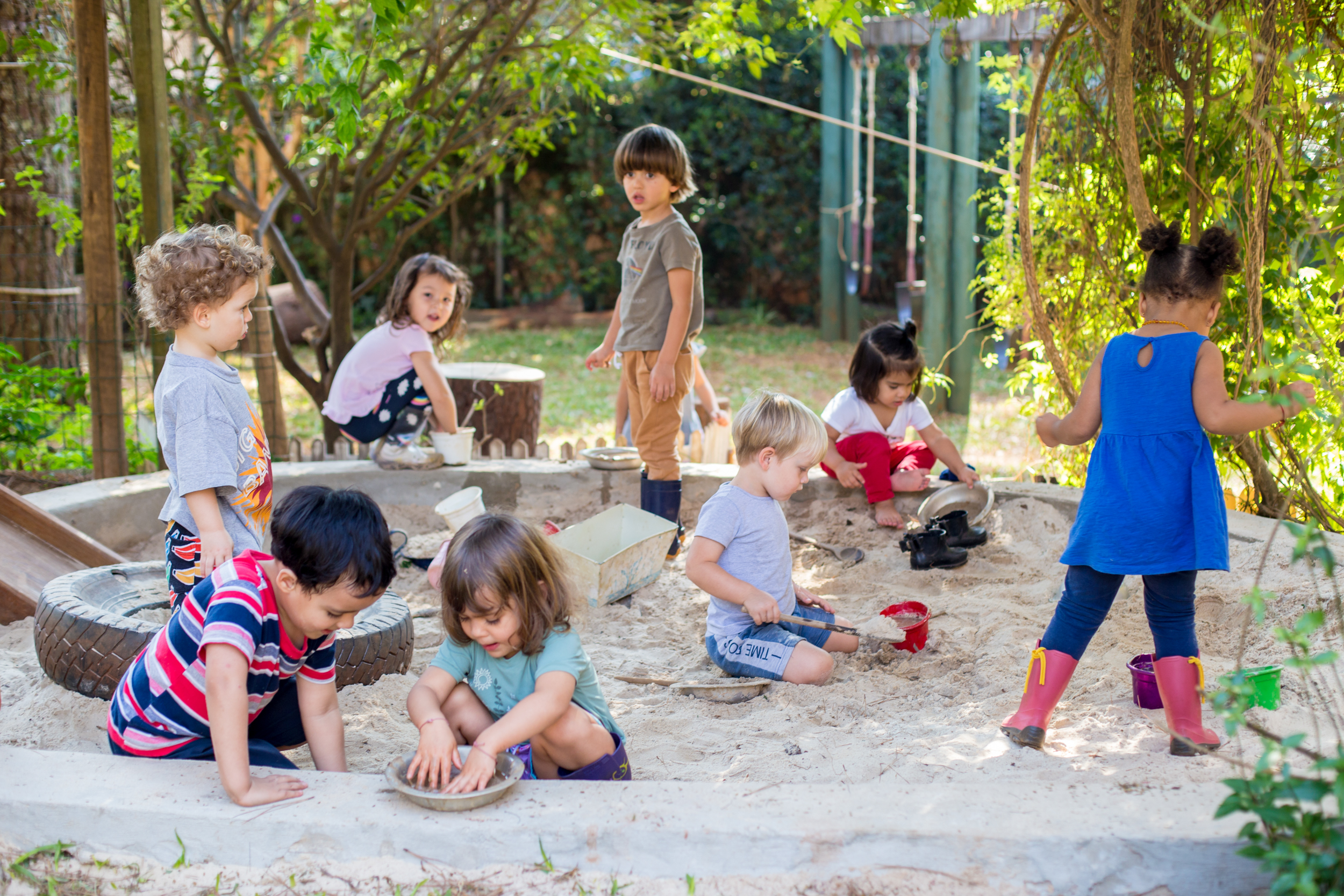Grupo de crianças pequenas brincando felizes na caixa de areia ao ar livre.
