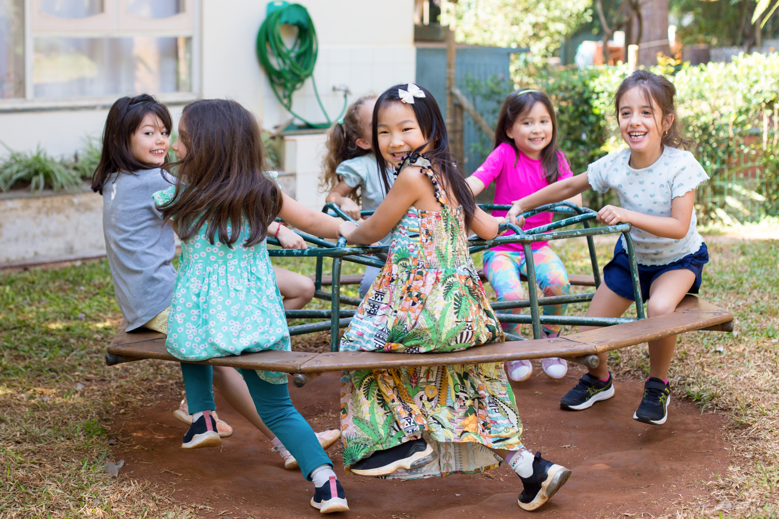 Grupo de crianças felizes brincando em um gira-gira ao ar livre no jardim de infância da Escola Waldorf Rudolf Steiner