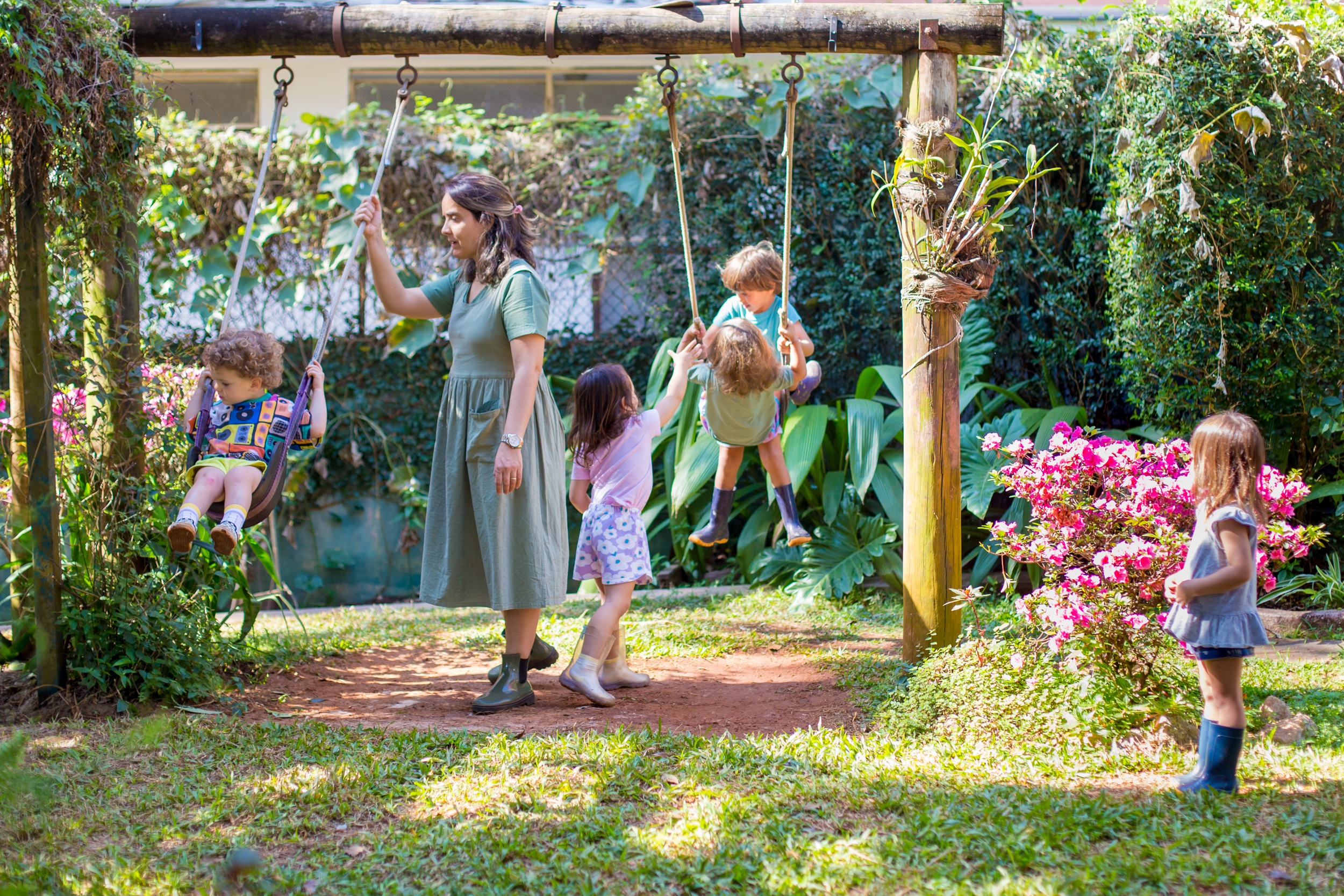 Professora empurrando criança em balanço com outras crianças brincando em jardim de infância da Escola Waldorf Rudolf Steiner