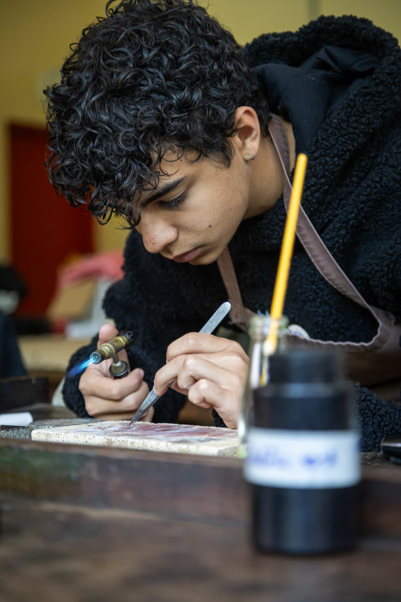 Aluno concentrado em trabalho manual com maçarico em oficina de arte ou artesanato na Escola Waldorf Rudolf Steiner.